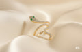 Gold snake-shaped earring with green gemstones on a beige fabric background